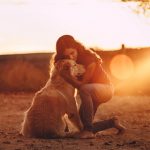 Una joven abraza cariñosamente a su perro mientras ambos disfrutan de una puesta de sol. La imagen captura un momento de conexión emocional y tranquilidad entre la chica y su mascota, destacando el vínculo especial entre humanos y perros.